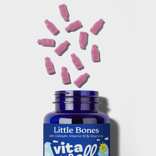 Blue supplement bottle labeled 'Little Bones' with pink gummy supplements on a light grey background
