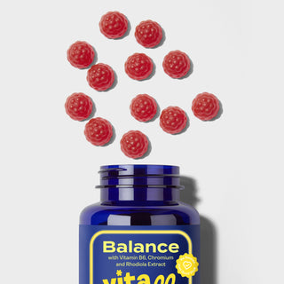 Blue supplement bottle labeled 'Balance' with red gummy supplements on a light grey background