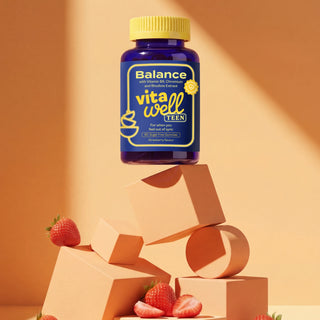 Balance vitawell Teen supplement bottle on geometric shapes with strawberries against an orange background