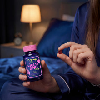 Person holding a bottle of 'Dream vitawell teen' vitamins in a bedroom setting.