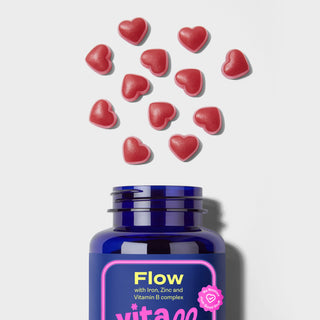 Blue bottle labeled 'Flow' with pink label and red heart-shaped gummies on a light grey background