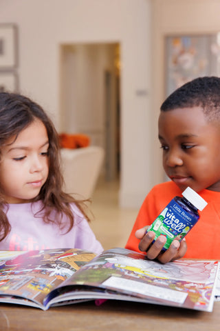 Two children looking at a magazine with one holding a bottle of Vitawell little bones vitamins.